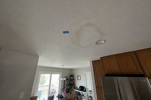 A dated piece of painter's tape marks the edge of a ceiling water stain in a lived-in kitchen