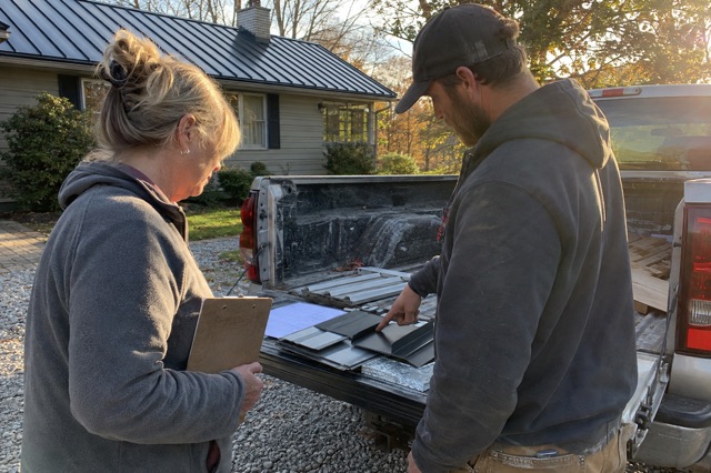 A homeowner and contractor review metal roof samples beside a work truck