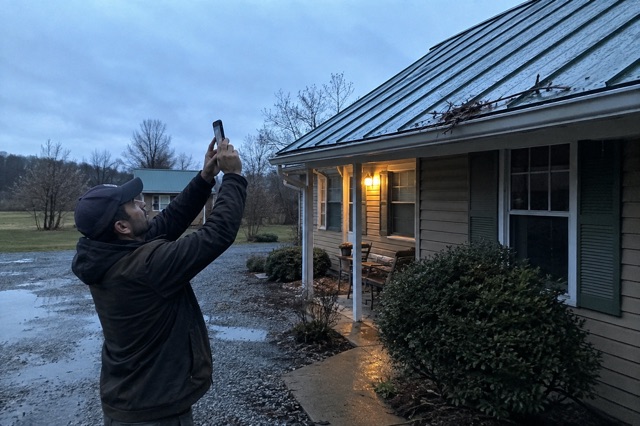 A homeowner safely photographs storm debris on a metal roof from the ground