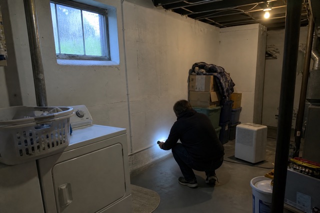 A homeowner uses a flashlight to check a basement wall for the source of a musty odor