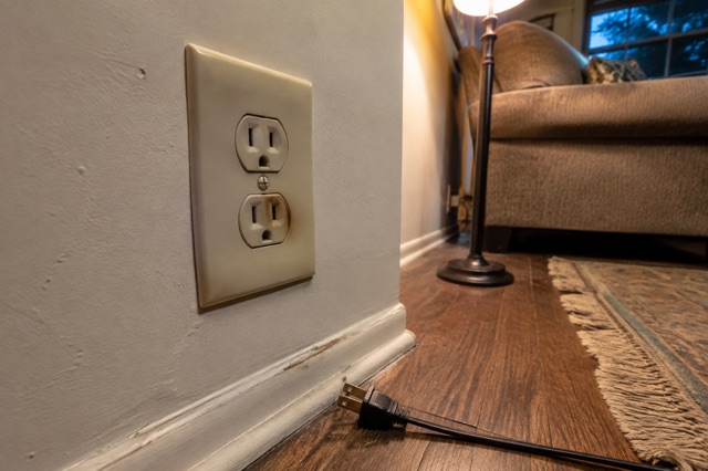 A slightly discolored wall outlet with its unplugged cord resting safely on the floor