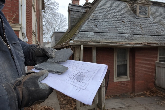 A slate-roof specialist shows natural slate pieces in front of an older slate roof