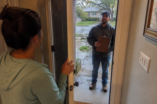 A homeowner speaks through a partly open door with an unexpected roofer after a storm