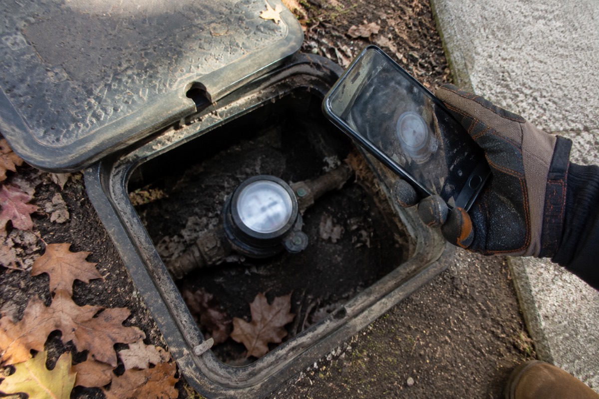 A homeowner photographs a residential water meter before checking the home for a hidden leak